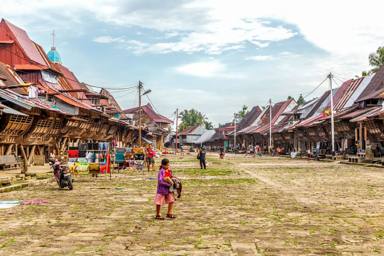 A wide view of an Indonesian village with people gathered near traditional buildings.