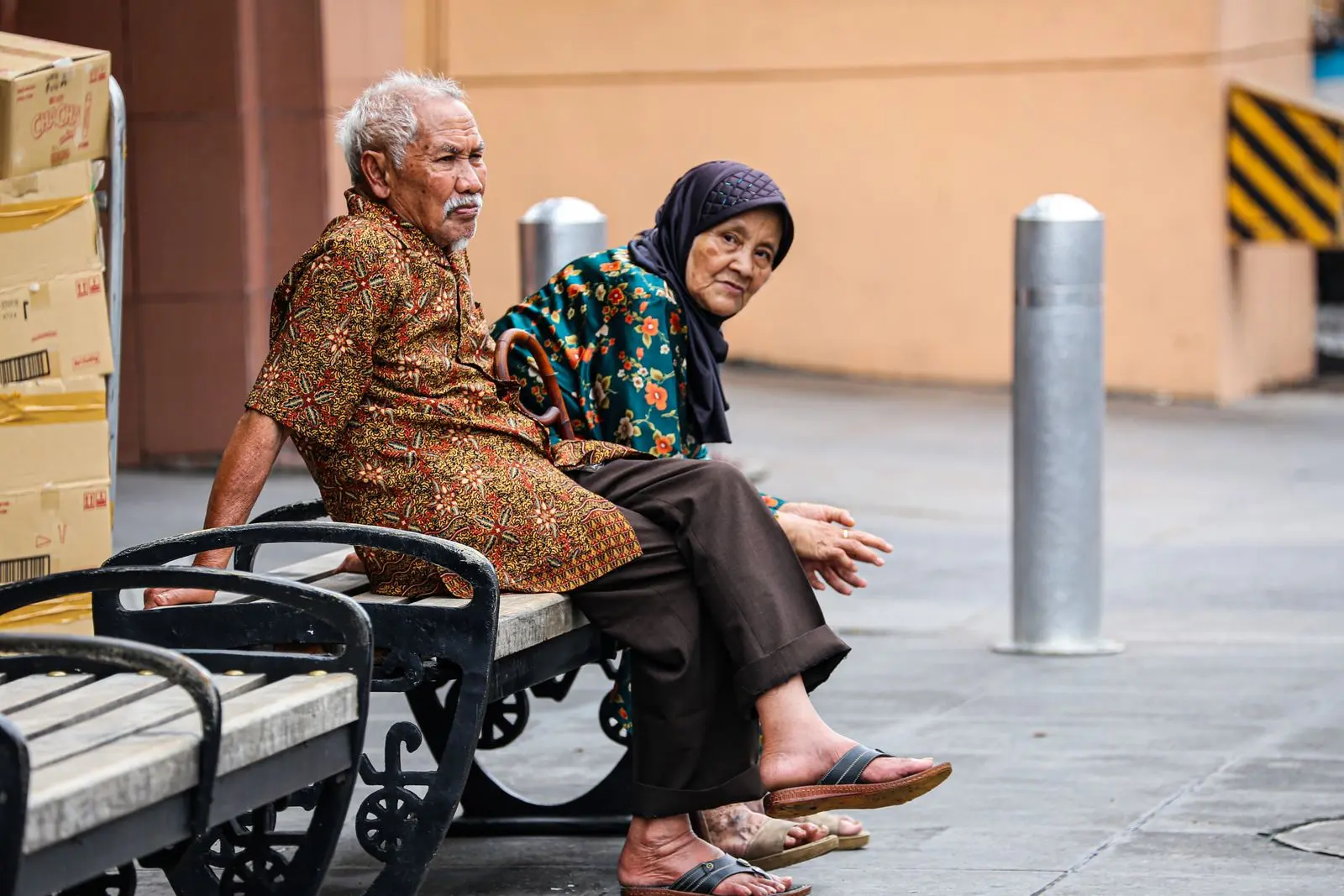 An older couple in patterned clothing resting on a bench in Yogyakarta, Indonesia.